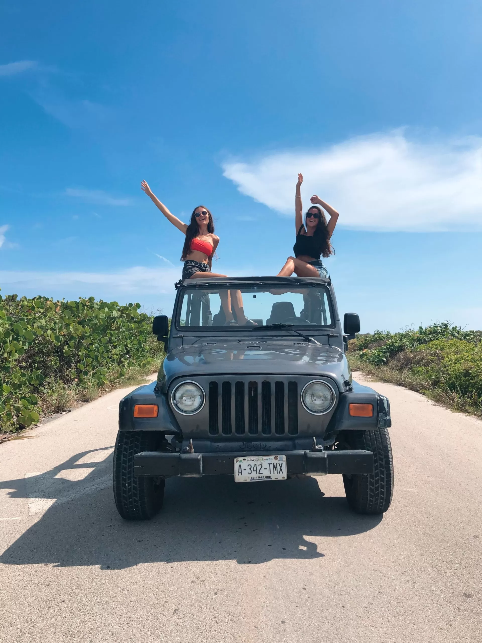 foto en la ruta de cozumel. con pau estamos paradas en los asientos de un jeep levantando los brazos.