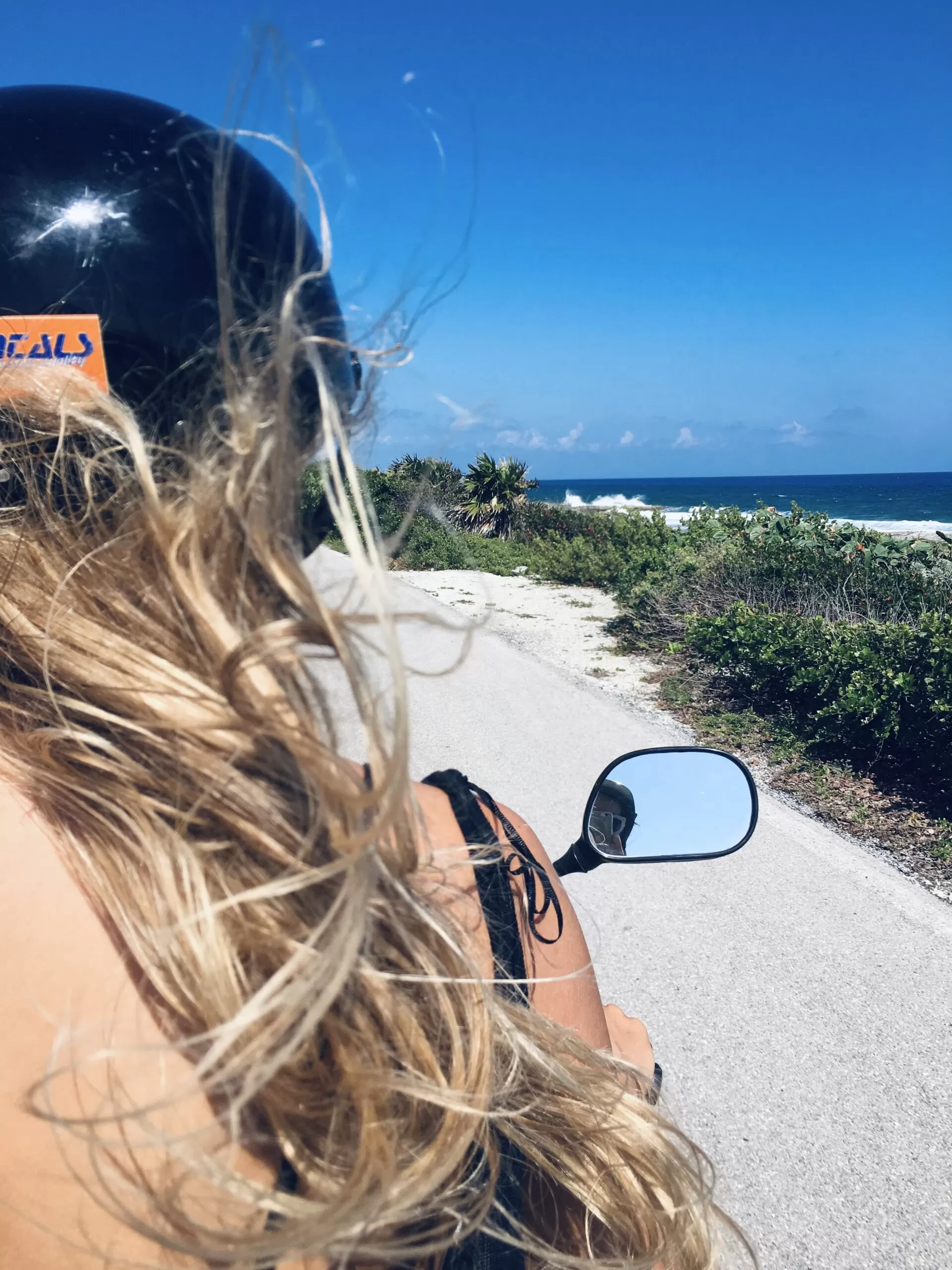 se puede ver una amiga mia manejando una moto por las calles de cozumel . de fondo el mar