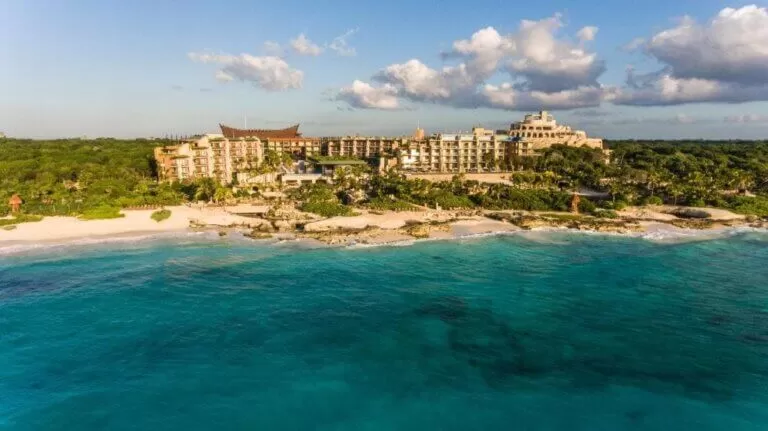 foto del hotel xcaret desde drone. tomada desde el mar. el hotel se ve muy grande, rodeado de selva. el agua del mar se ve turquesa