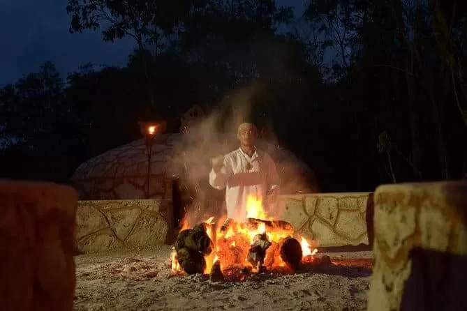 es de noche. hay un hombre maya atras de un fogon admirando el fuego