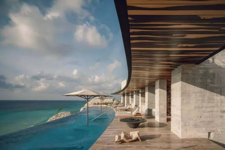 foto del hotel "La Casa de la Playa by Xcaret". se puede ver una pileta con borde infinito. unos camastros en la galeria del hotel. y el mar al lado