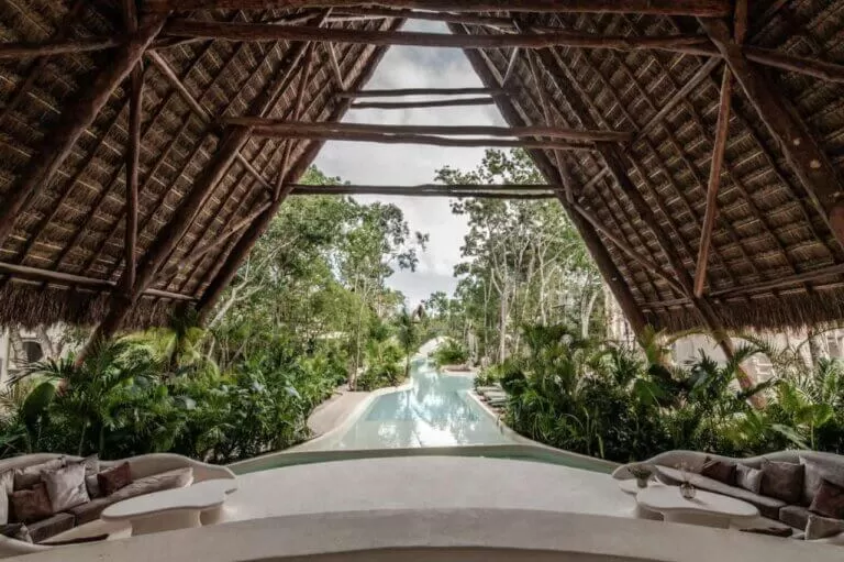 foto del hall del hotel milam , tulum. techos altos de paja en forma de V. y una gran selva atras.
