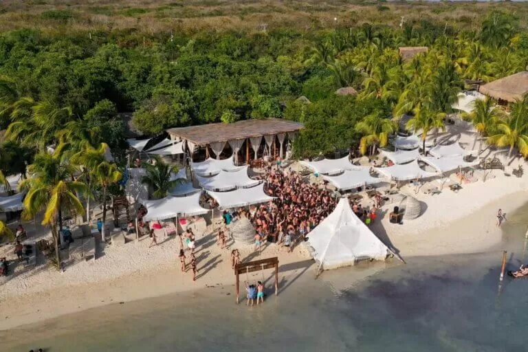 fiesta en una playa de isla mujeres. foto tomada desde drone. se ve mucha gente en la playa y varias carpas blancas.