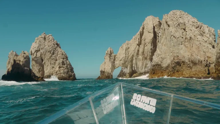 foto tomata desde el bote transparente en el agua. de fondo se ve el famoso arco de cabo san lucas (unas formaciones rocosas en forma de arco)