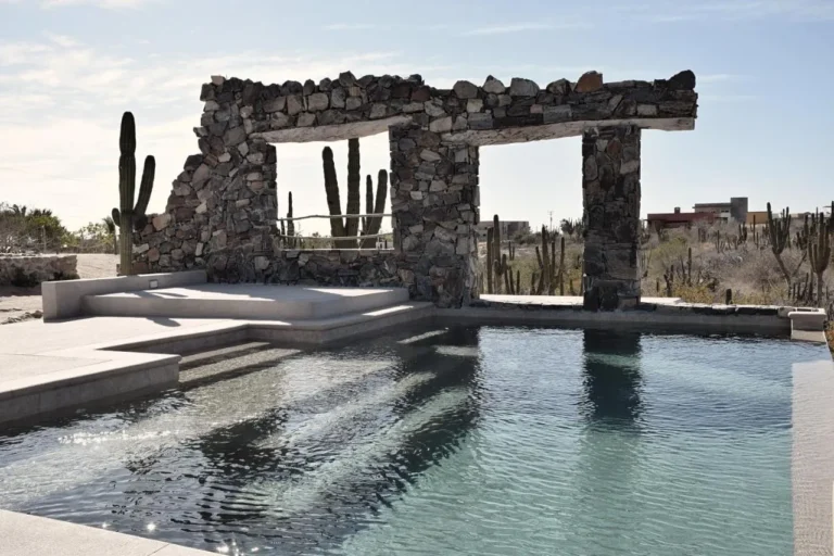 se puede ver la piscina del hotel desierto azul. alrededor se ve el desierto y cactus. y una estructura de piedra alrededor.