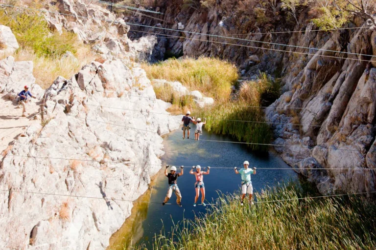 Persona haciendo tirolesa en Los Cabos, deslizándose por cables sobre cañones y disfrutando de vistas panorámicas del paisaje desértico.