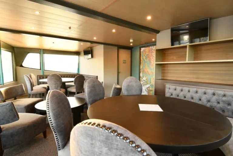 salon del barco vip en el calafate. se ve una mesa y unas sillas acolchonadas alrededor